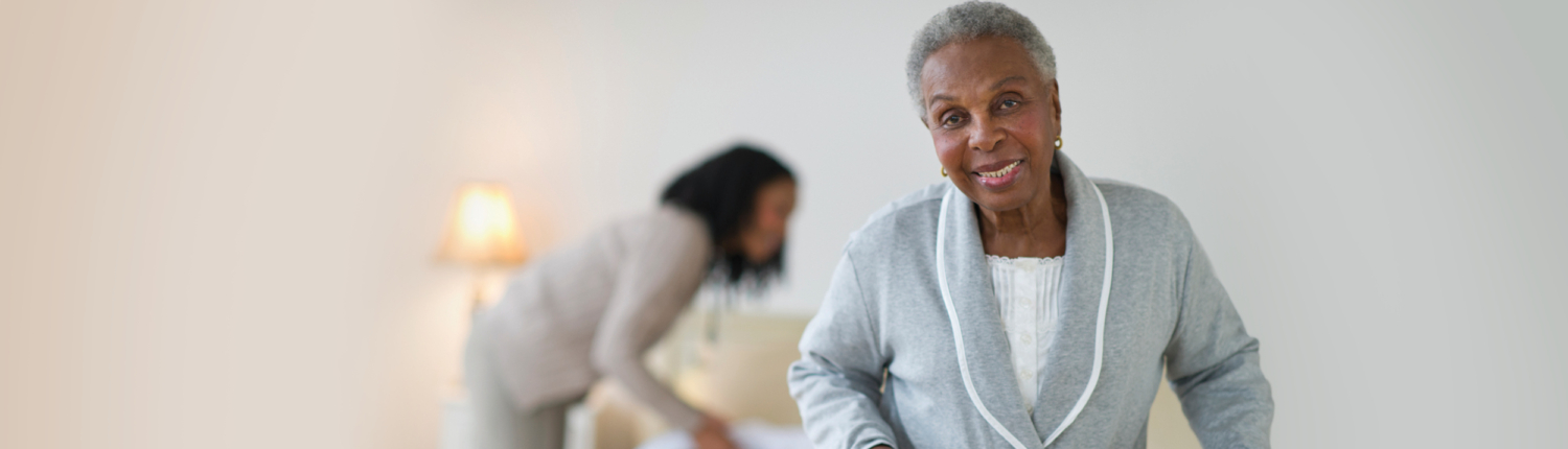 smiling senior woman in a bedroom with younger woman in the background