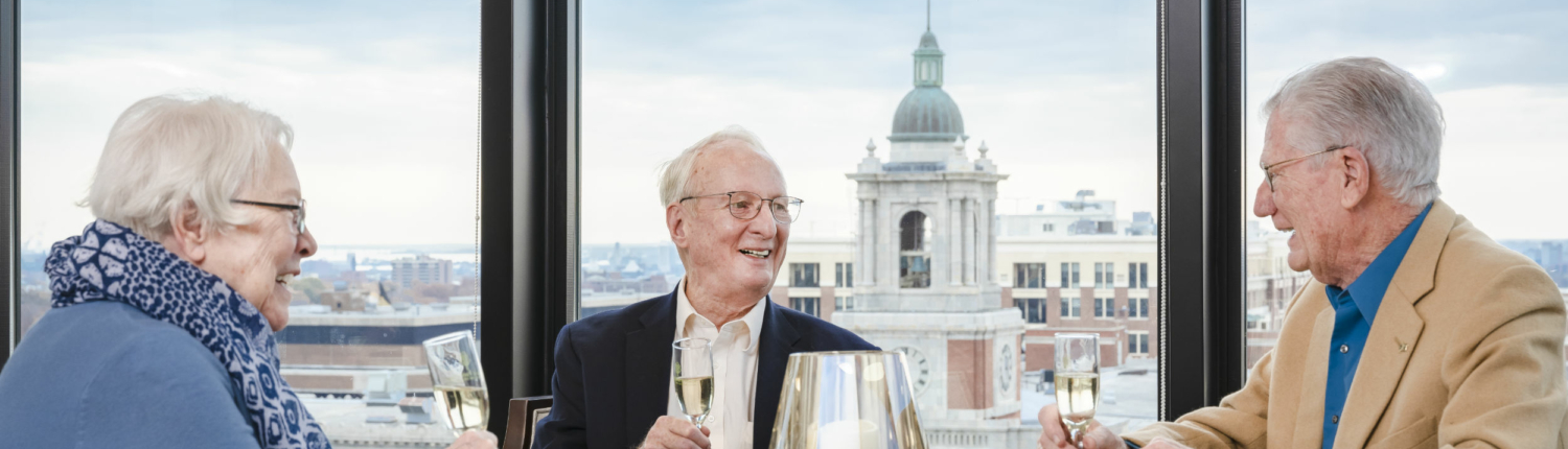 three Baltimore senior living residents enjoying champagne next to large city-view windows