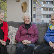 three senior women sitting together on a couch and smiling