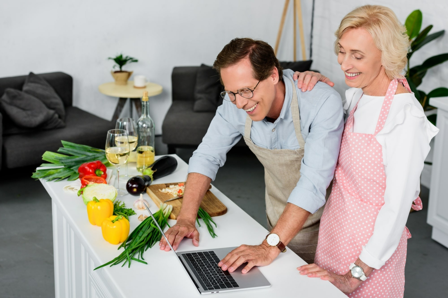 Image of a senior couple looking up a recipe on a laptop while preparing a healthy dinner. 