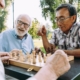 3 happy senior men sitting around a chess board at a table outdoors