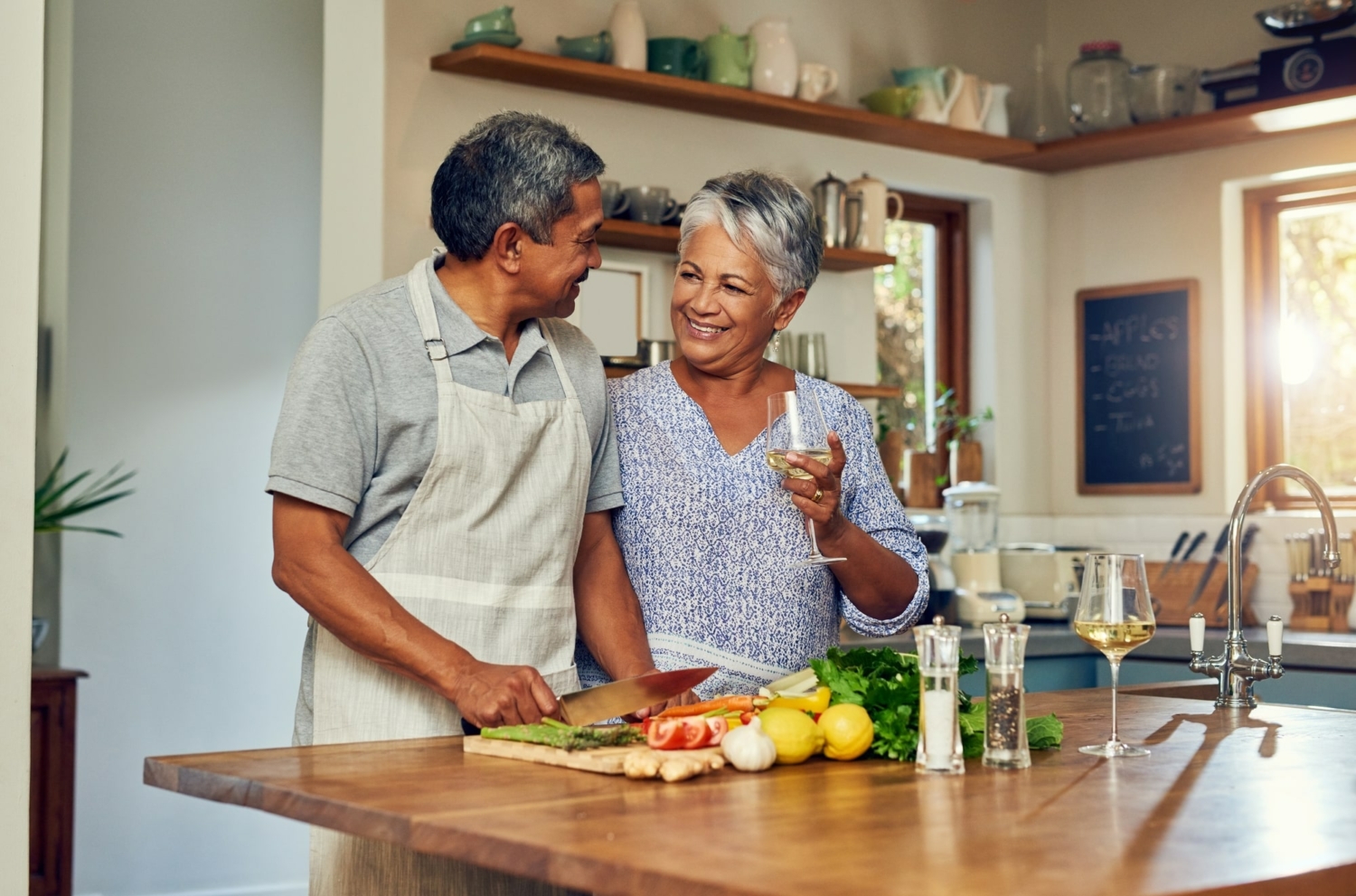 senior couple standing together in a kitchen and smiling while cutting up vegetables as they meal prep for seniors