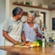 senior couple standing together in a kitchen and smiling while cutting up vegetables as they meal prep for seniors